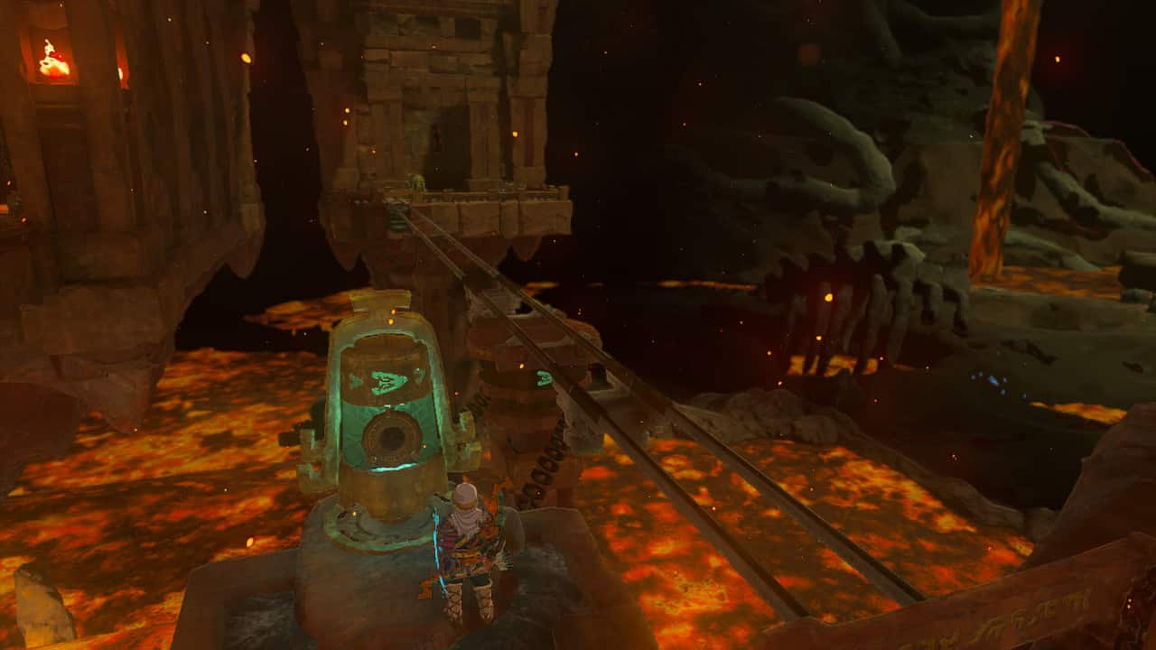Tears of the Kingdom Fire Temple: Link next to a bell-shaped switch with minecart tracks leading to a distant building.