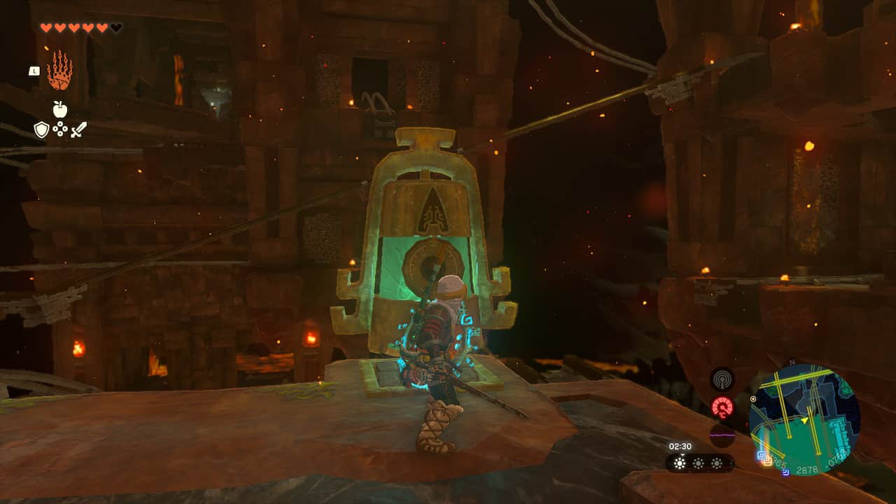 Tears of the Kingdom Fire Temple: Link next to a bell-shaped switch with multiple minecart tracks and buildings in the background.