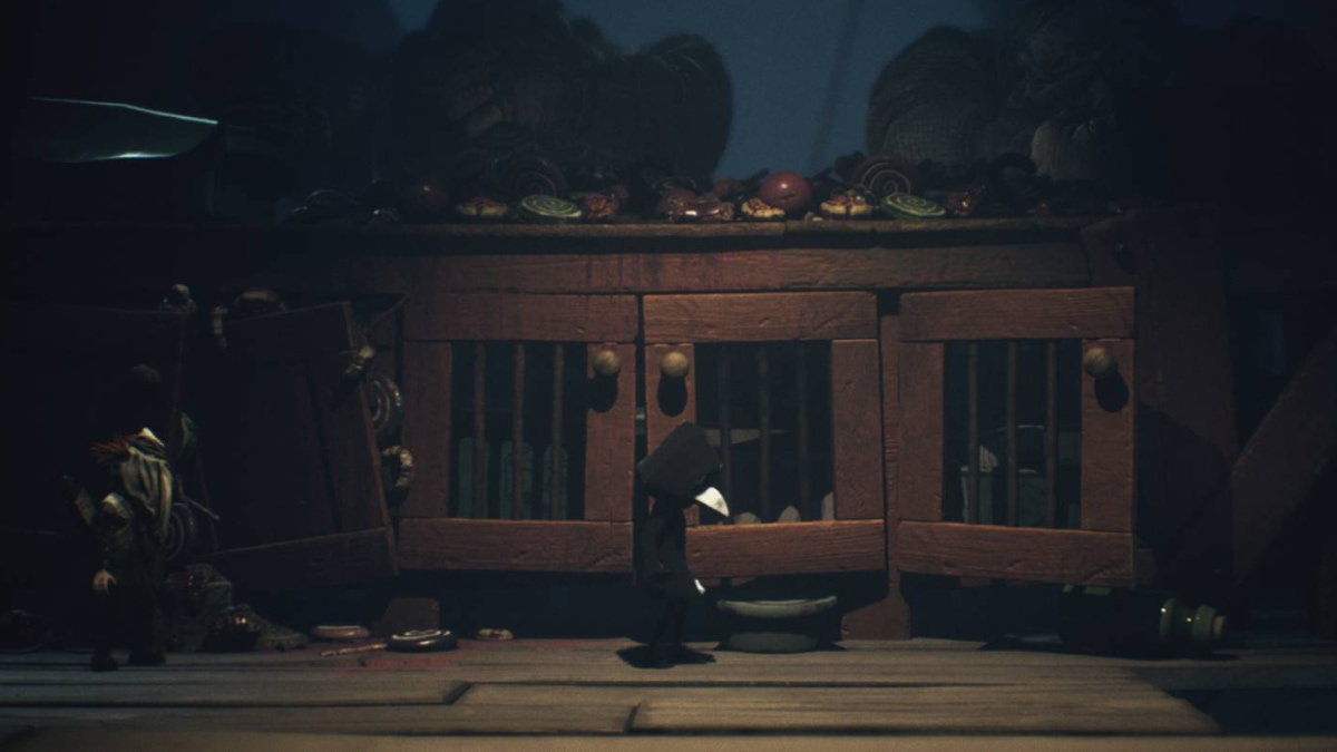 Two small characters walking past a large wooden cabinet filled with food in Little Nightmares 3