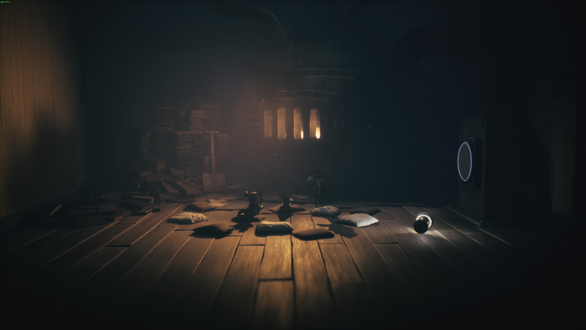 Small characters stand before a glowing furnace in Little Nightmares 3, surrounded by scattered pillows and a dimly lit room