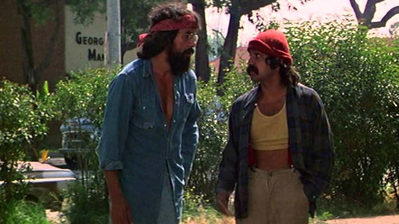 Two men with mustaches and red headbands having a discussion in a warzone outdoors.