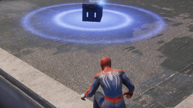 Spider-Man 2 stands in front of a chest containing tech parts.