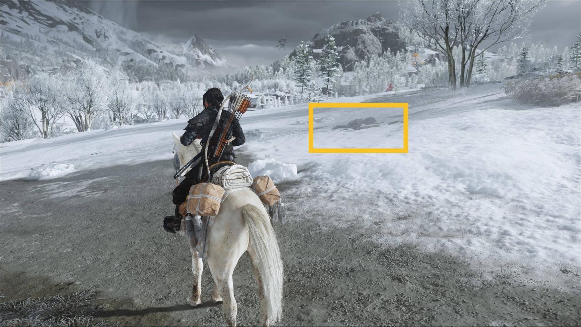 The character in the game Ghost of Yotei rides a horse through a snowy landscape surrounded by trees and mountains under a cloudy sky, creating a sense of winter adventure