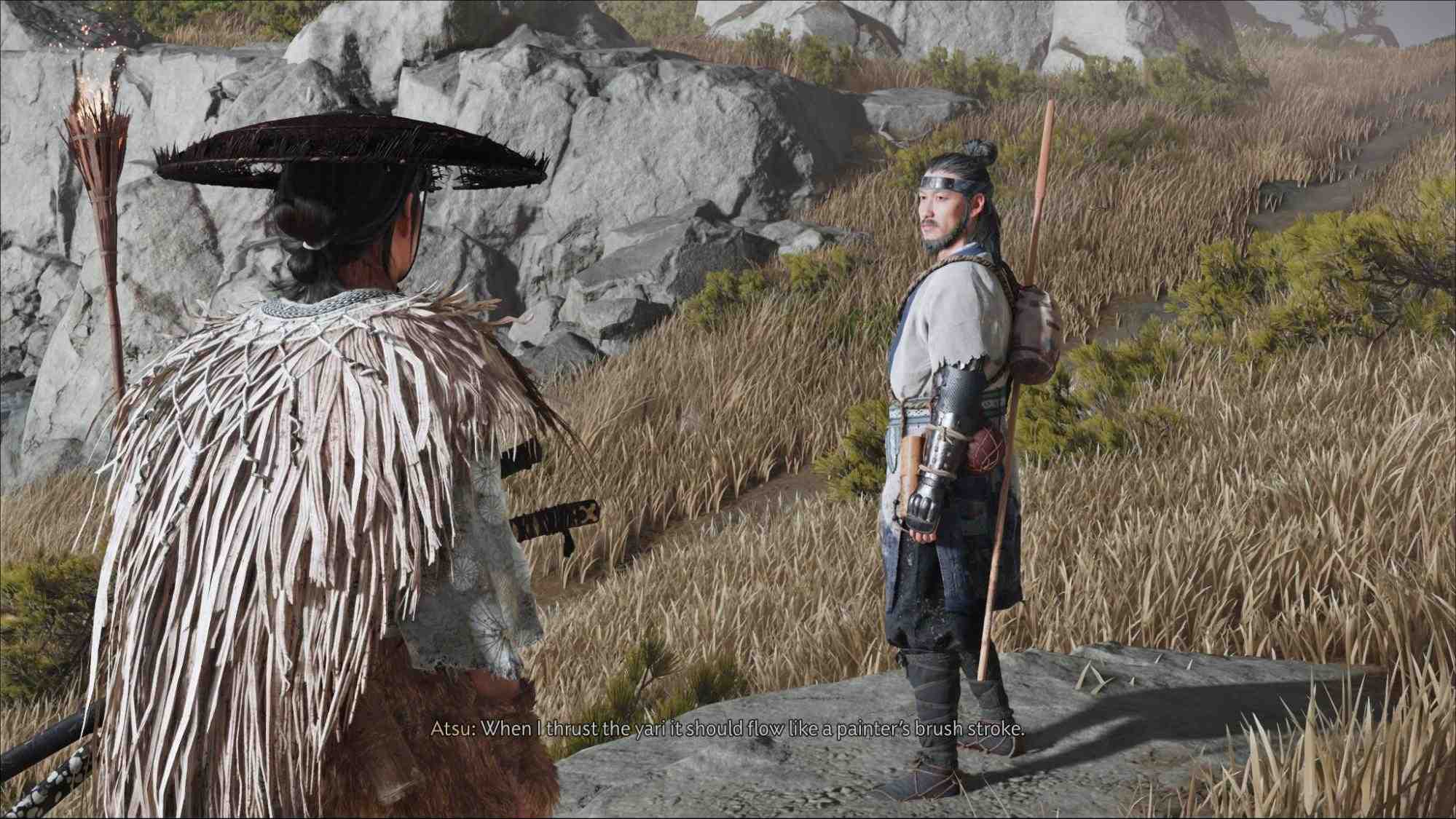 Ghost of Yotei screenshot showing Atsu, the main protagonist, speaking with a Sensei on a rocky hillside, with tall grass and a torch nearby.