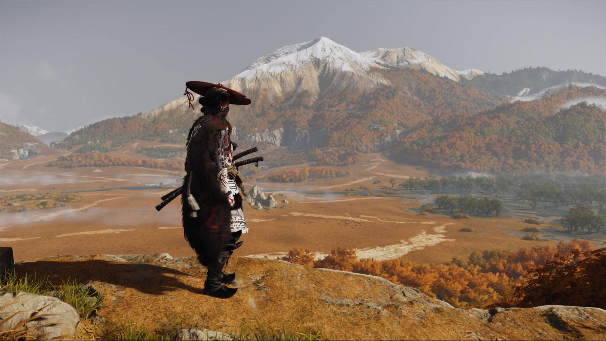 Warrior looks out over autumn plains and snowy mountains in Ghost of Yotei