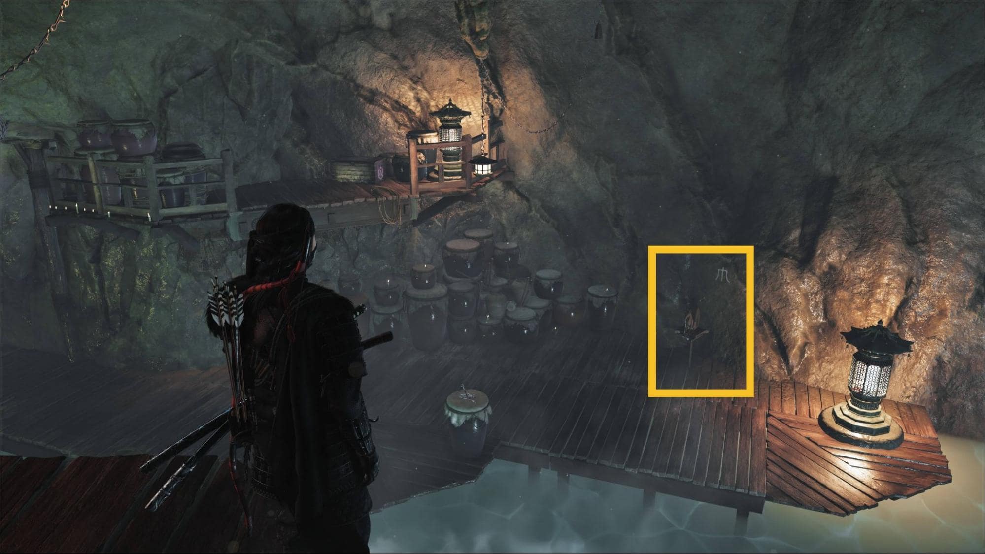 Player inside the Ghost of Yotei Snow Drift Springs Shrine cave, looking at the switch marked in yellow beside the wooden platform and jars