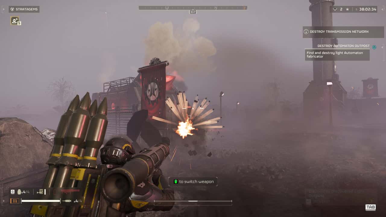 A player in a first-person shooter game fires an airburst rocket from a launcher at a distant enemy base, causing an explosion amidst a desolate, foggy landscape.