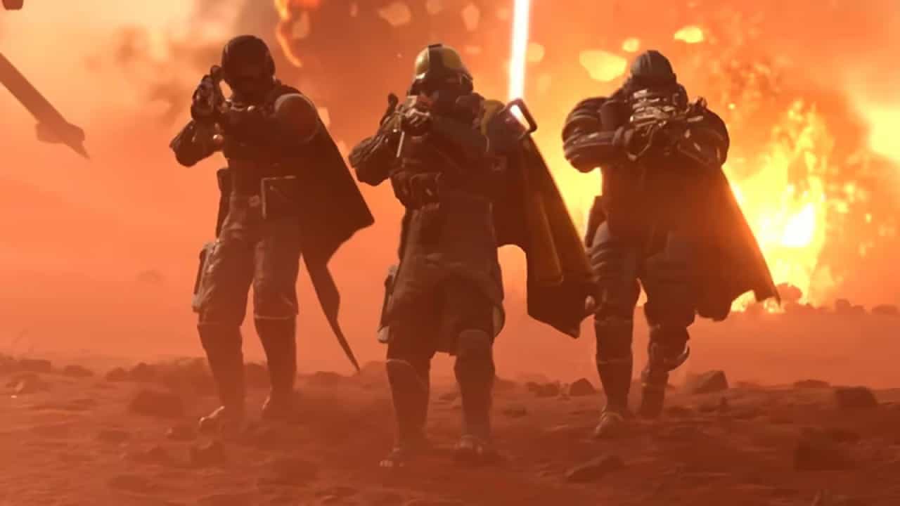 Three futuristic Helldivers 2 soldiers in armor advance through a smoky, explosive battlefield.