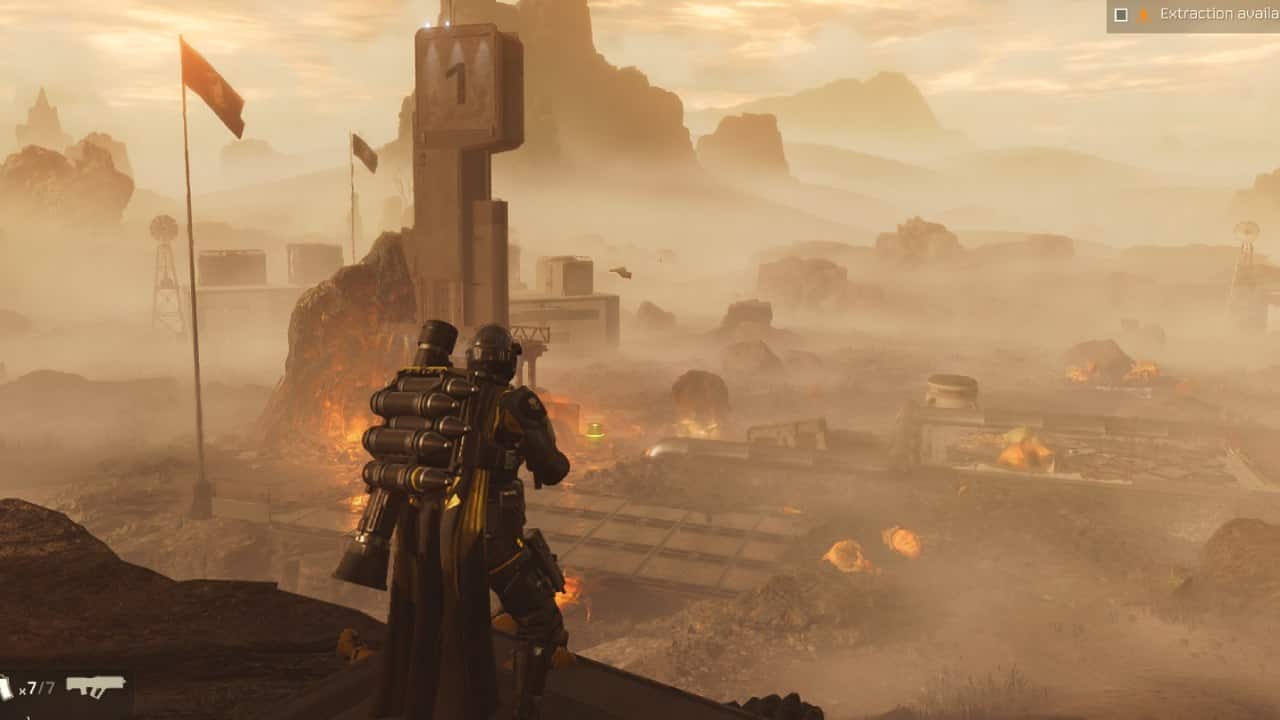 A Helldivers 2 soldier in futuristic armor overlooks a misty, war-torn landscape with fires and scattered debris under an orange sky.