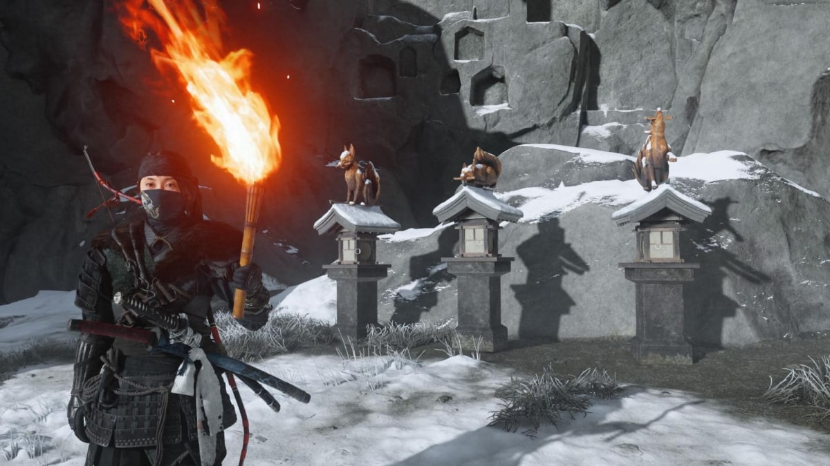 Warrior holding a burning torch beside fox lantern statues in the snowy Ghost of Yotei Snow Drift Springs Shrine area