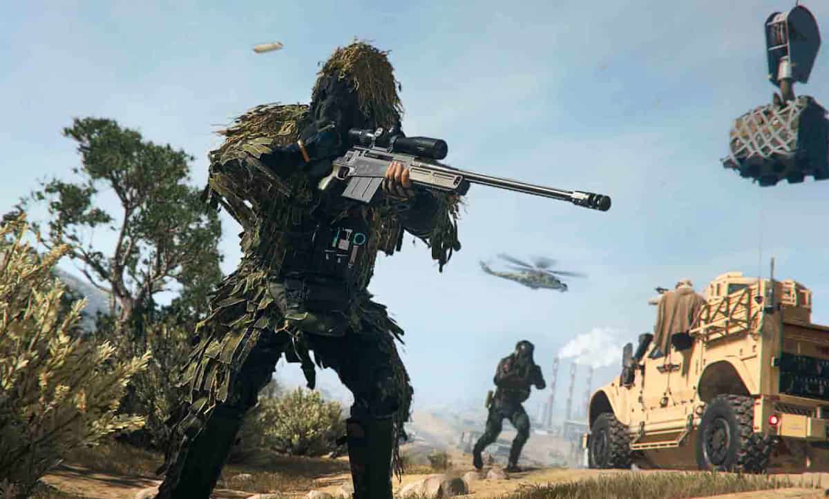 How to reduce recoil in Warzone 2 and MW2: A soldier in a camouflage readies a sniper rifle in the foreground while an armoured jeep and a helicopter drive towards an oil refinery in the background.