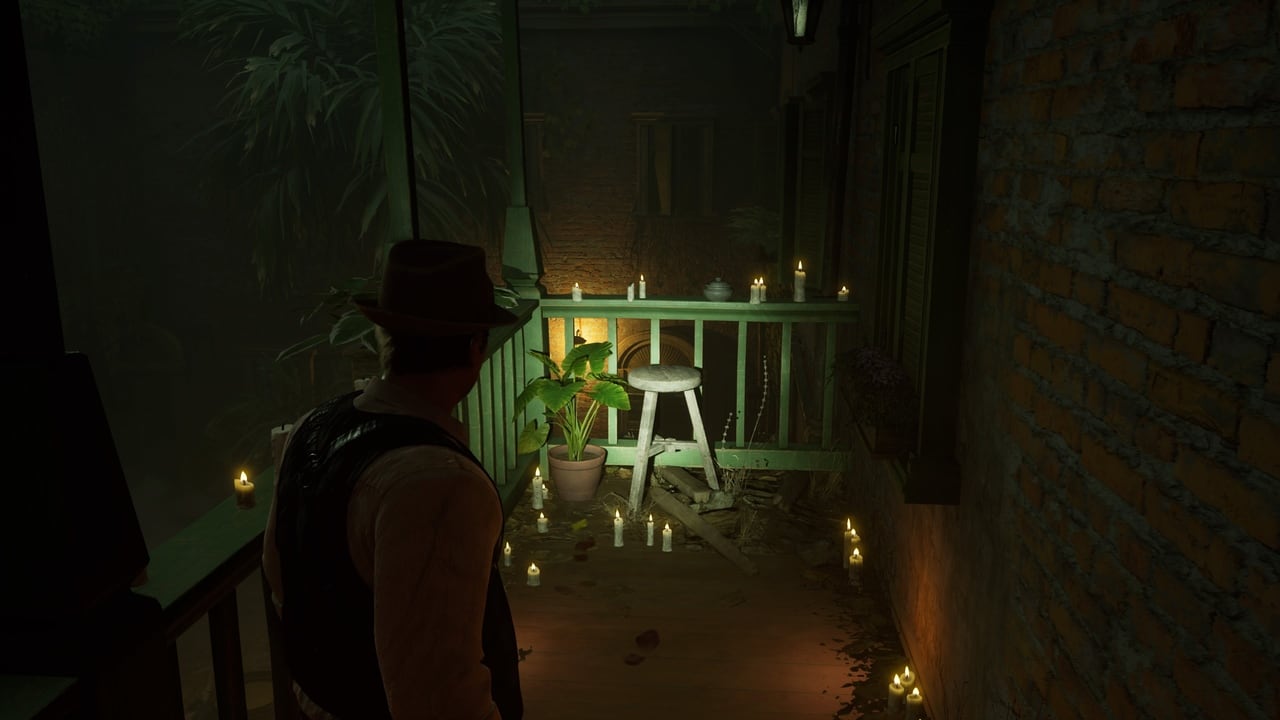 A person in a hat gazes alone at a dimly lit balcony adorned with candles and plants at night.