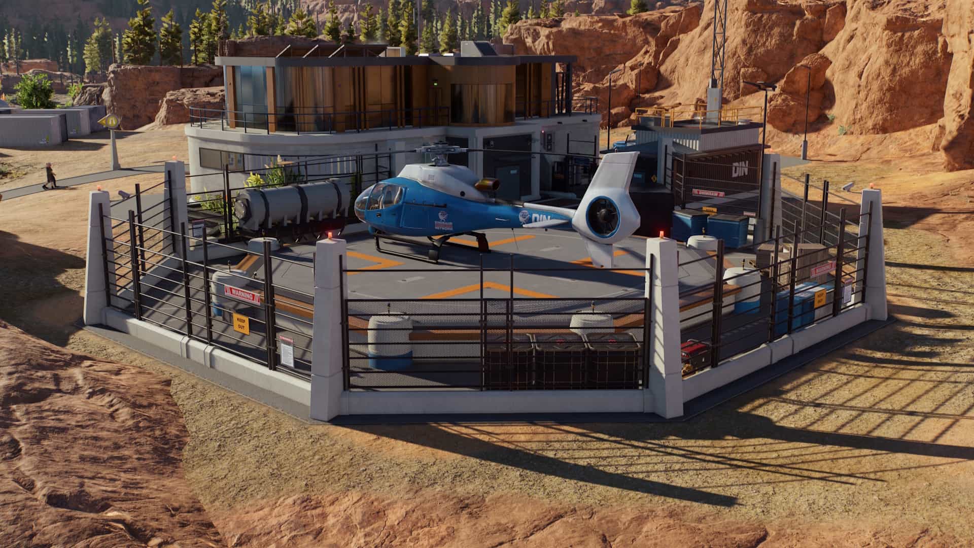 A blue capture team helicopter sits on the landing pad outside the operations center in Jurassic World Evolution 3’s desert park.