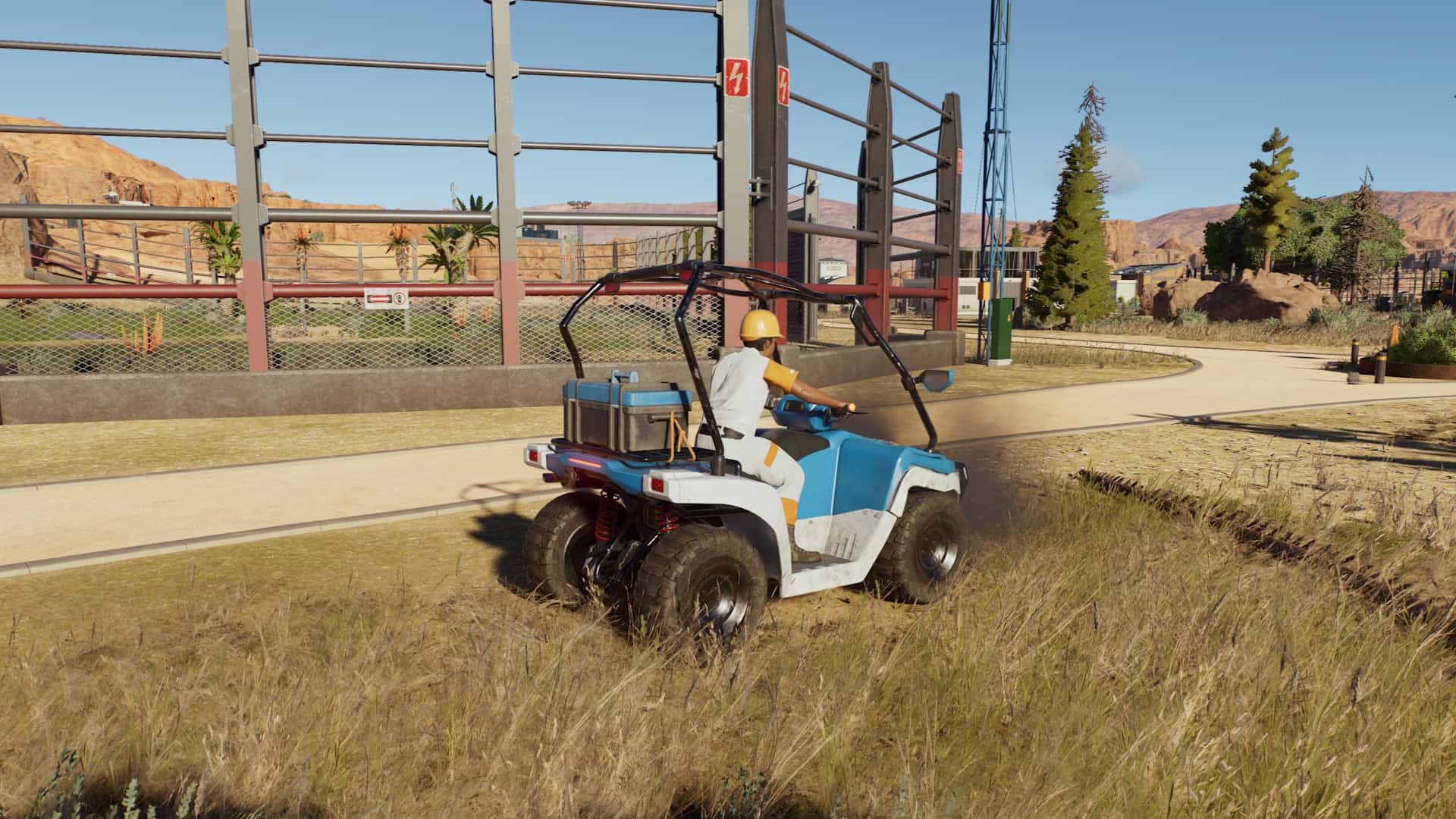 A park ranger drives an ATV near an electrified dinosaur enclosure in Jurassic World Evolution 3’s desert map.