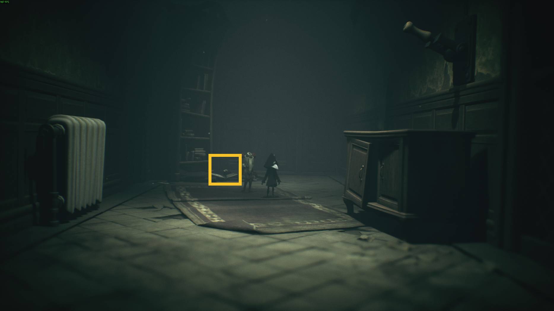 Small hidden figure near a fallen book in the dark hallway of Little Nightmares 3