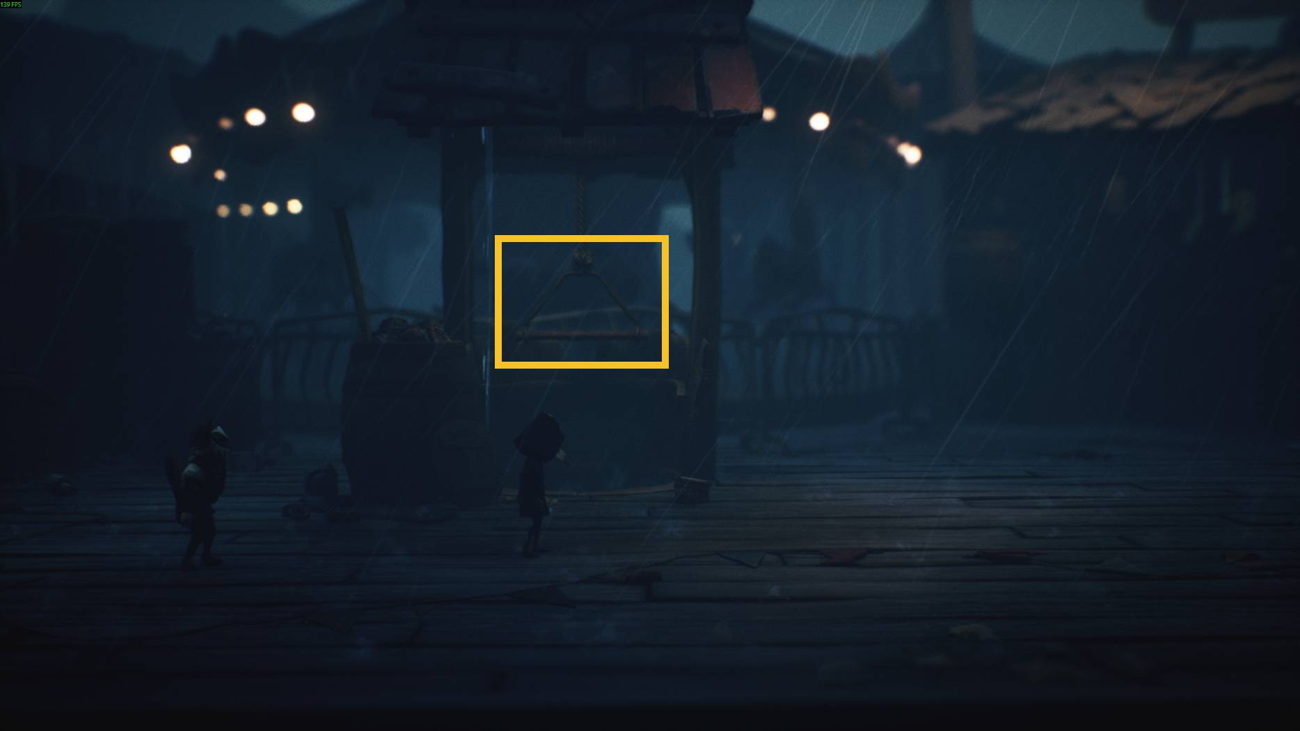 Two small characters at a rain-soaked carnival pause before a well with a hanging triangle handle in Little Nightmares 3