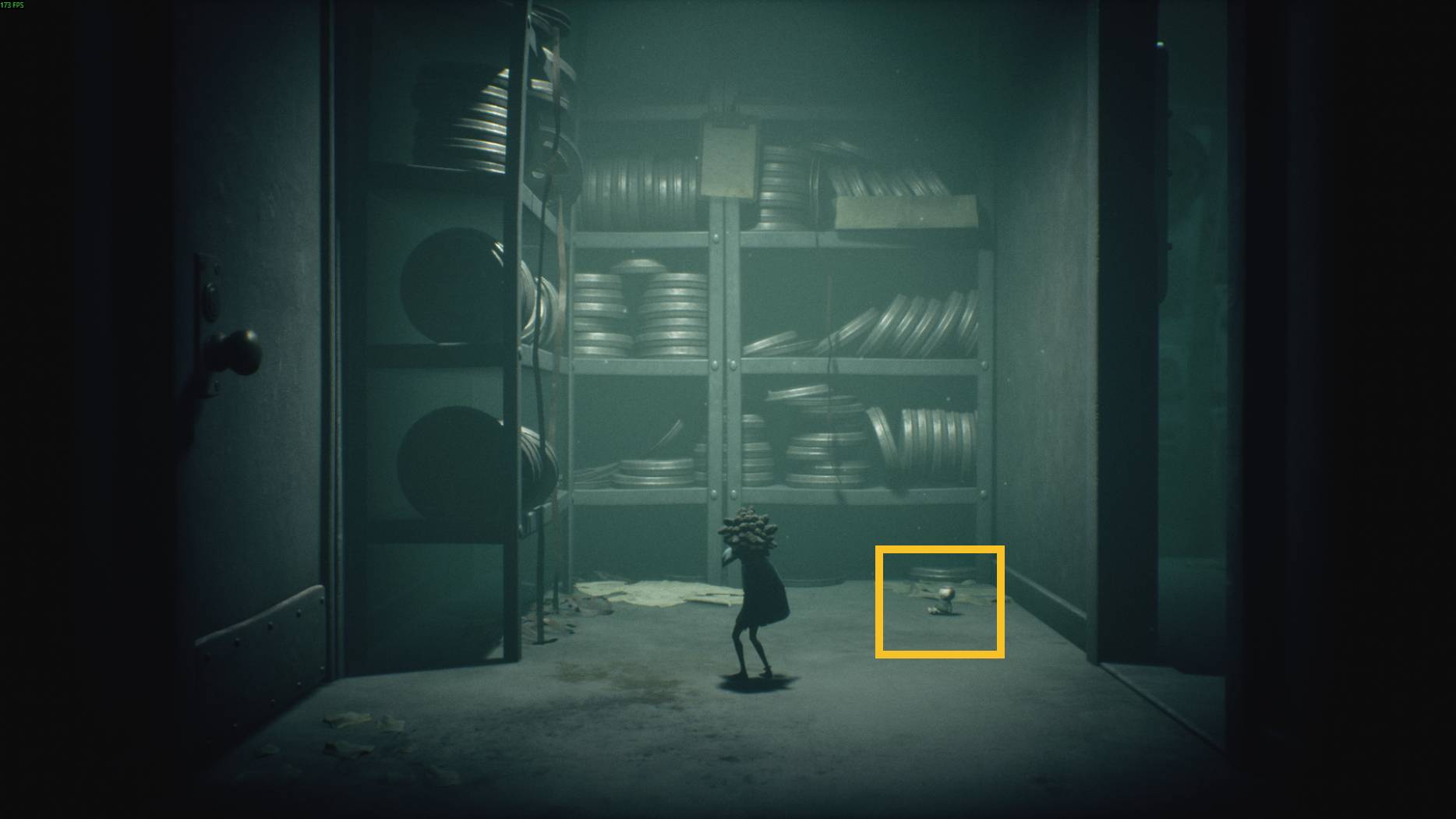 A small character explores a dark archive room filled with stacked film reels in Little Nightmares 3.