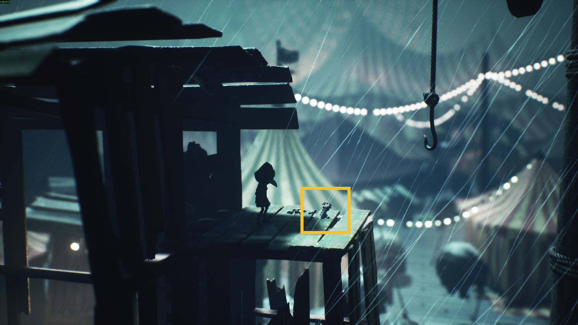 A small character on a rainy rooftop next to a tiny hidden figure, with carnival tents glowing in the background in Little Nightmare