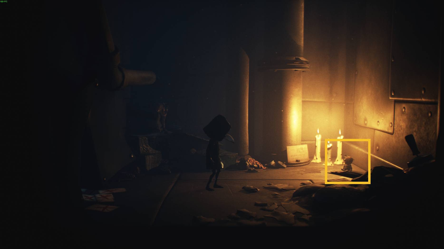 A secret small figure in Little Nightmares 3 is sitting on the floor near burning candles in a dark industrial room