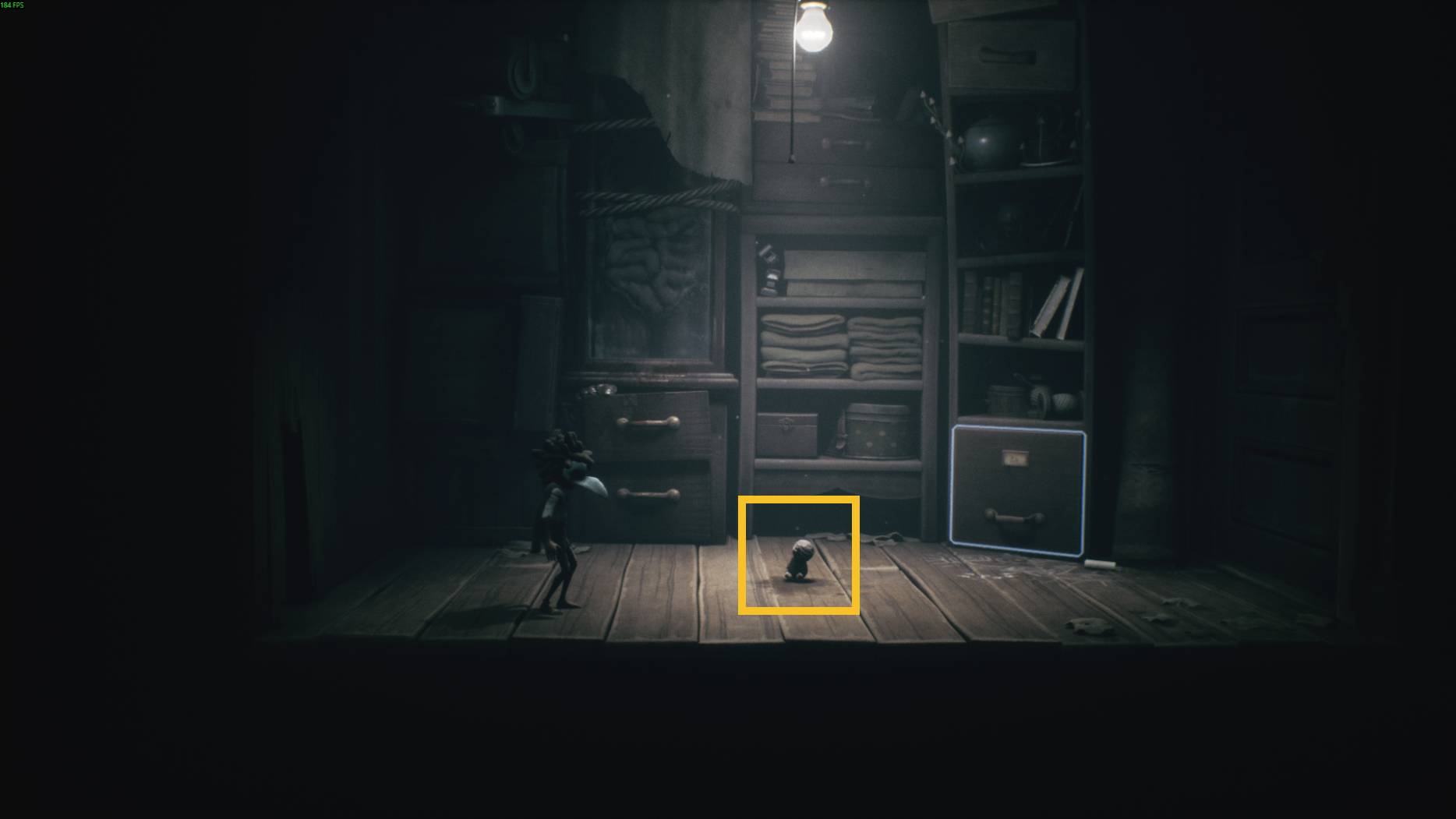A doll-like figure appears on the wooden floor of a dim storage room, with shelves full of folded items and drawers in Little Nightmares 3.