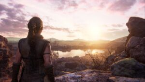 senua's saga hellblade 2 release time - a woman stands on a rocky outcrop looking at the sun over water.