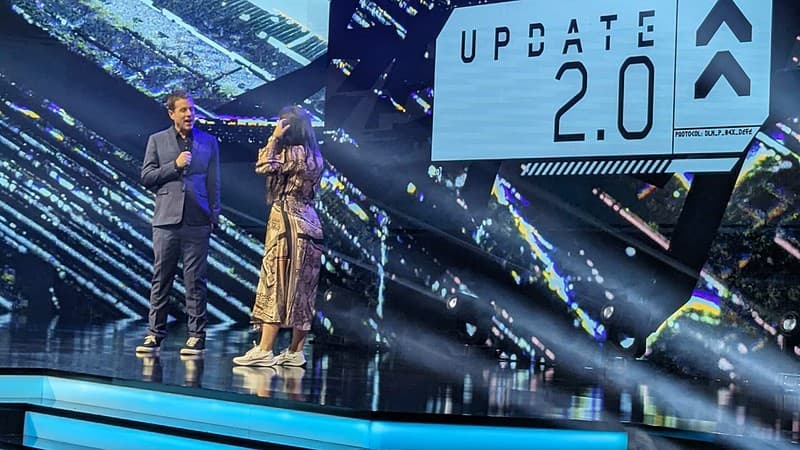 Two people standing on stage announcing the Cyberpunk 2077 2.0 update for current-gen consoles and PC.