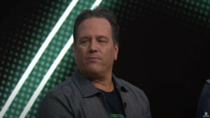 A middle-aged man with short, dark hair wearing a gray shirt and a dark jacket, who trends on Twitter, standing in front of a green digital backdrop.