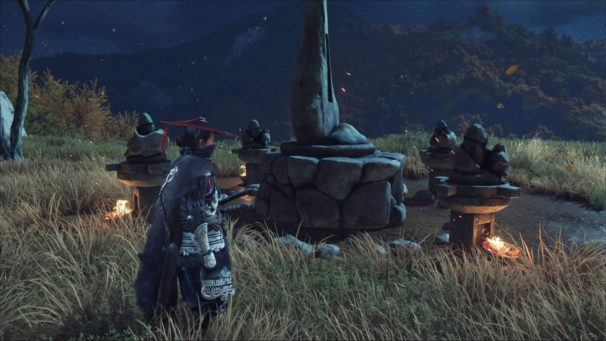 A warrior in traditional armor stands in a field at night, surrounded by stone lanterns and statues in Ghost of Yotei