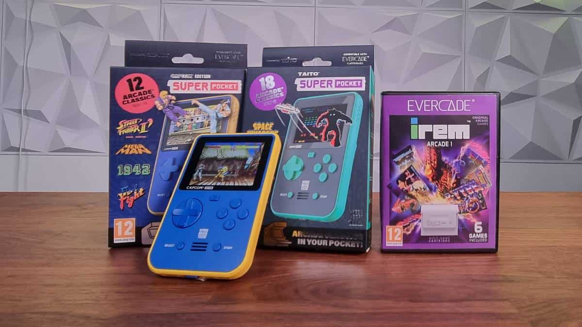 Two Super Pocket packaging boxes, a yellow and blue Super Pocket console rests in front. To the side there is an Irem arcade cartridge box. Captured by Videogamer.