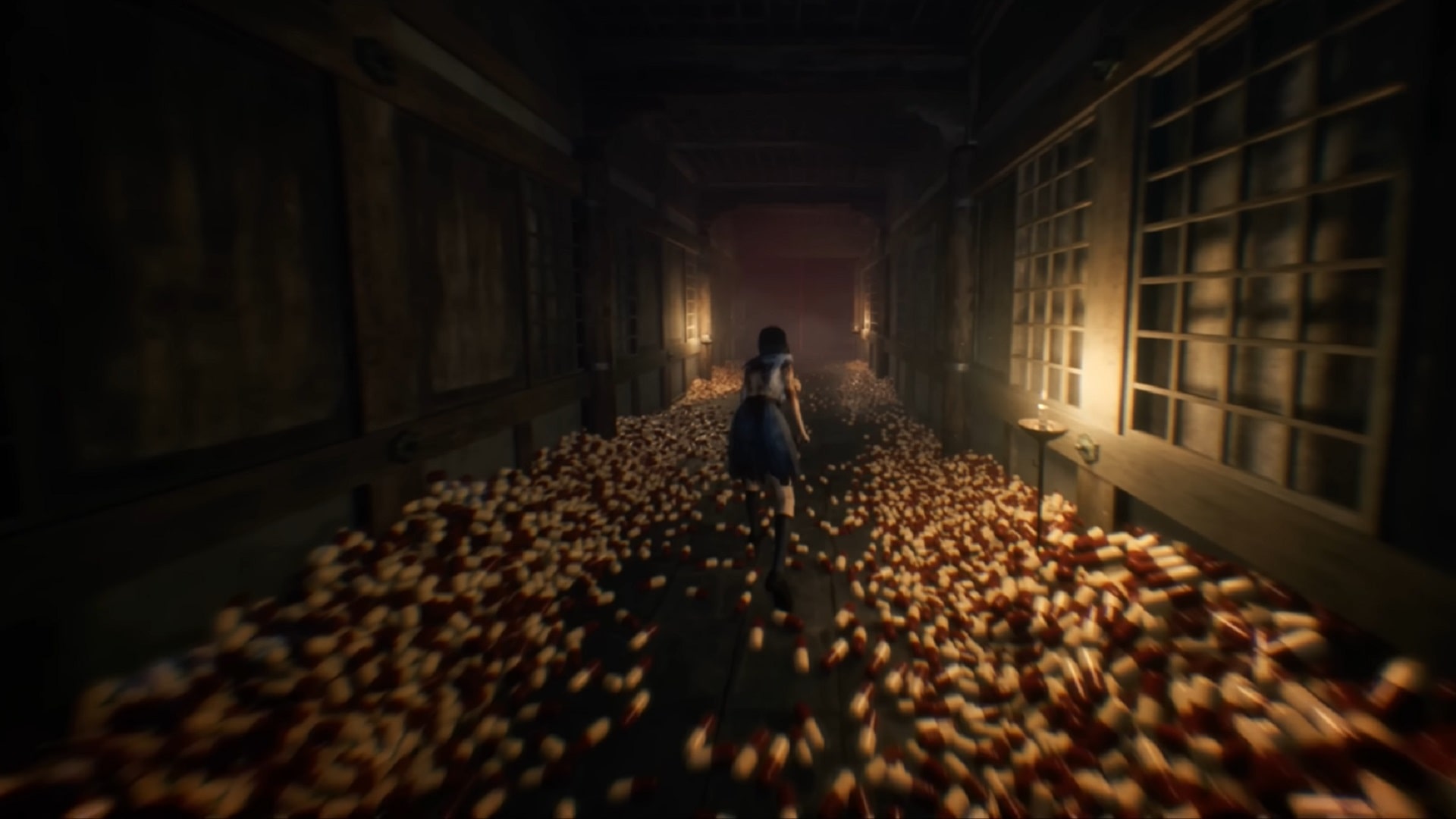A girl in a blue school uniform runs down a dimly lit hallway in Silent Hill f, surrounded by hundreds of red and white pills covering the floor.