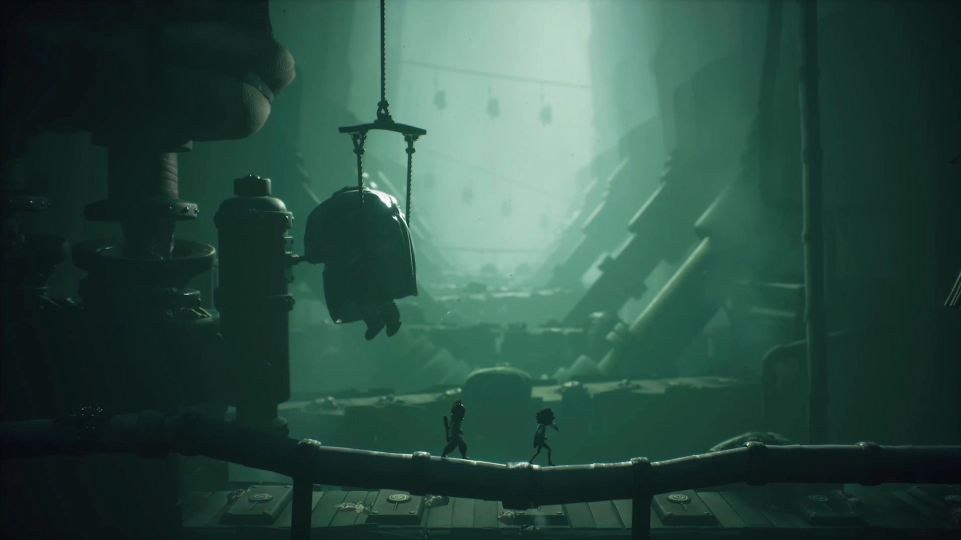 Low and Alone walk through a dark, mechanical tunnel filled with hanging figures in Little Nightmares 3