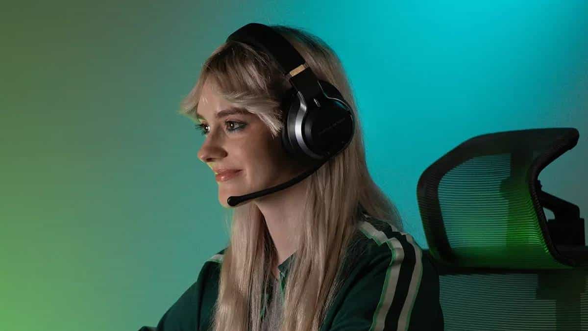 A woman wearing a headset is showcasing the Turtle Beach Stealth Pro gaming headset in front of a green screen.