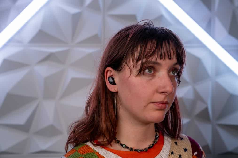A woman wearing earphones in front of a neon wall.
