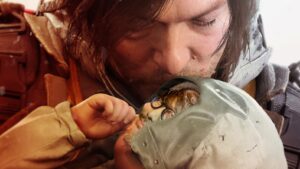 Hideo Kojima as a baby being kissed on the forehead by Death Stranding 2 Norman Reedua