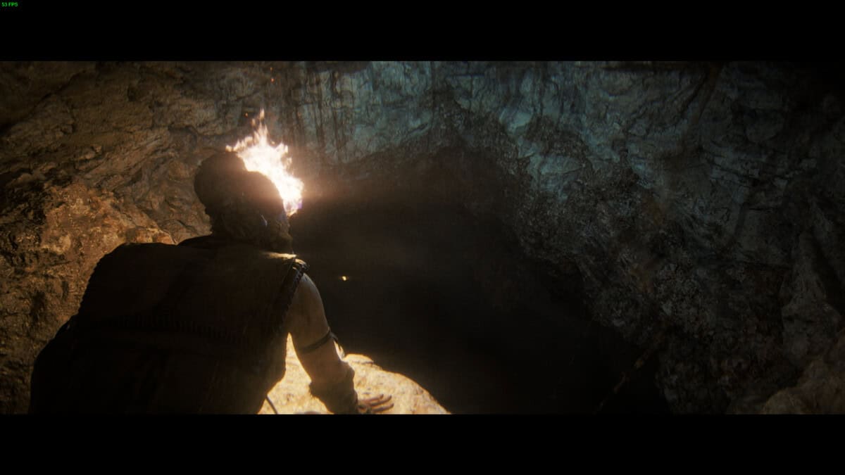 Hellblade 2 Hidden Faces locations: Senua holding a torch looks into a dark underground cave.