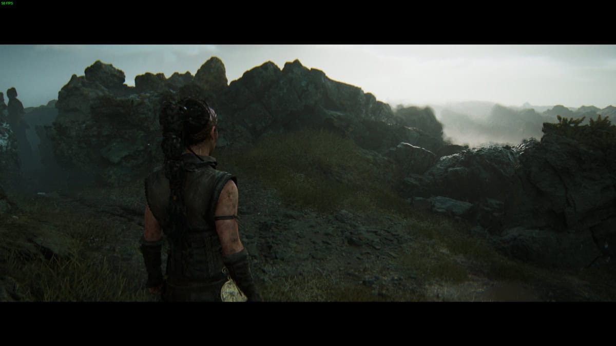 Hellblade 2 Hidden Faces: Senua stands in a rugged, rocky landscape under a cloudy sky.