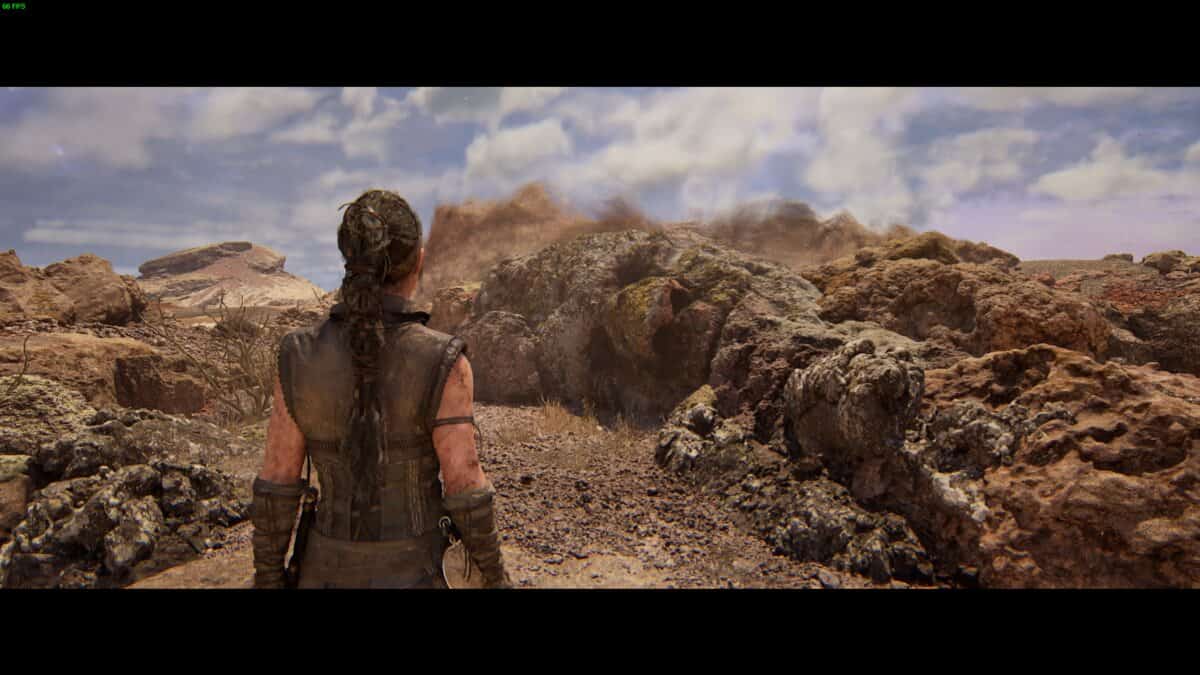 Hellblade 2 Hidden Faces locations: Senua stands in a rocky, barren landscape under a cloudy sky.