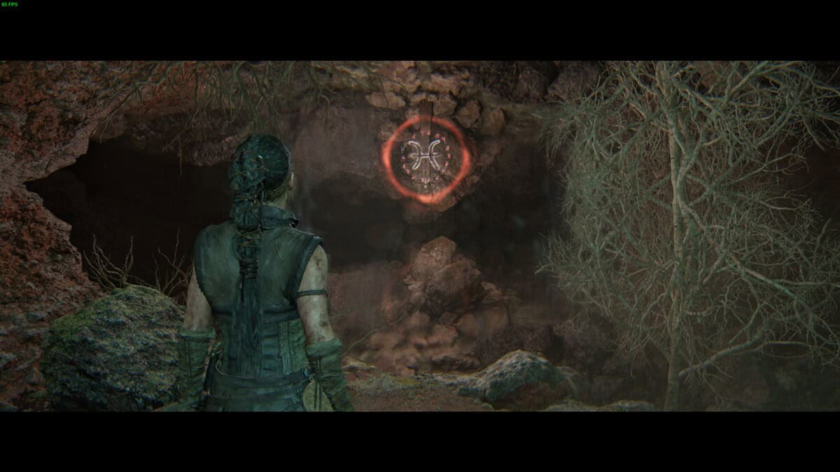 Hellblade 2 Lorestangir locations: Senua stands in a rocky, dimly lit cave facing a glowing rune symbol.
