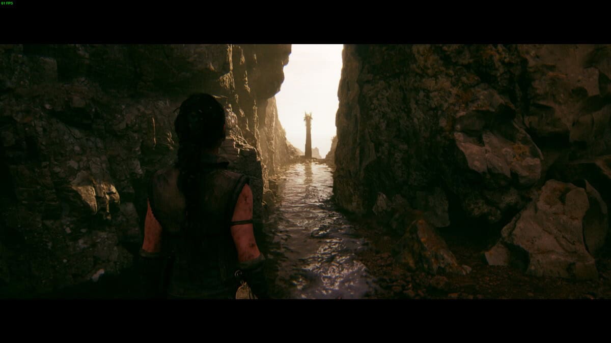 Hellblade 2 Lorestangir locations: Senua a rocky canyon, facing a narrow passage leading towards a totem.