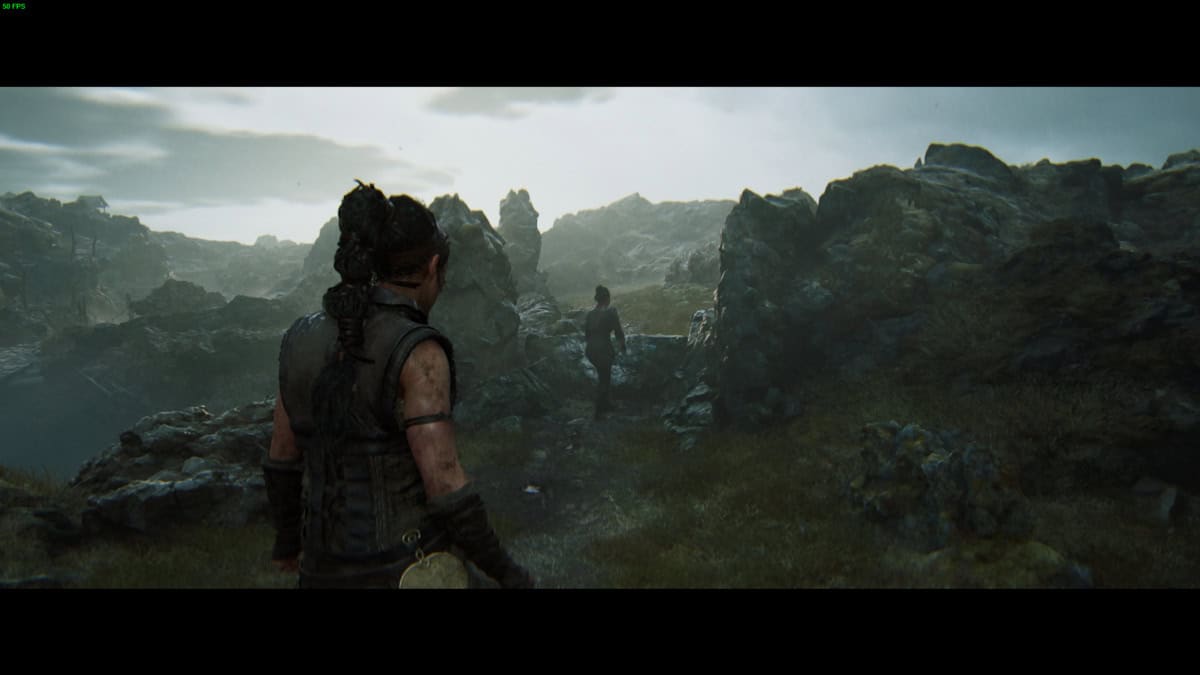 Hellblade 2 Lorestangir locations: Senua stands in a rocky, misty landscape looking towards a figure.