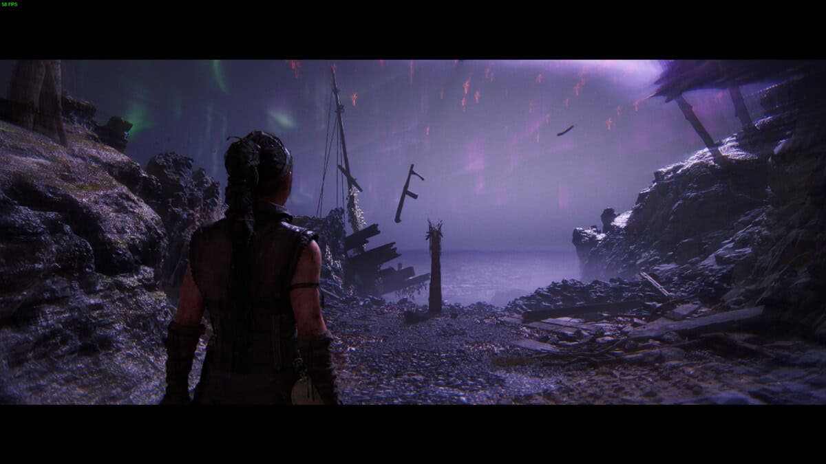 Hellblade 2 Lorestangir locations: Senua stands on a rocky shore at night, looking at a misty sea with purple skies.