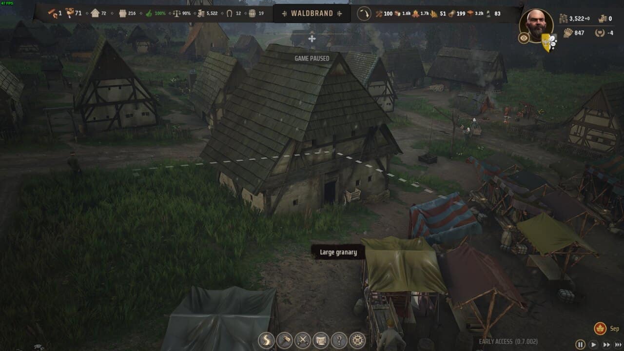 Manor Lords buildings: Screenshot from a medieval-themed video game showing a paused scene with various detailed Manor Lords buildings, market stalls, and a character avatar labeled "waldbrand" in the upper right corner.