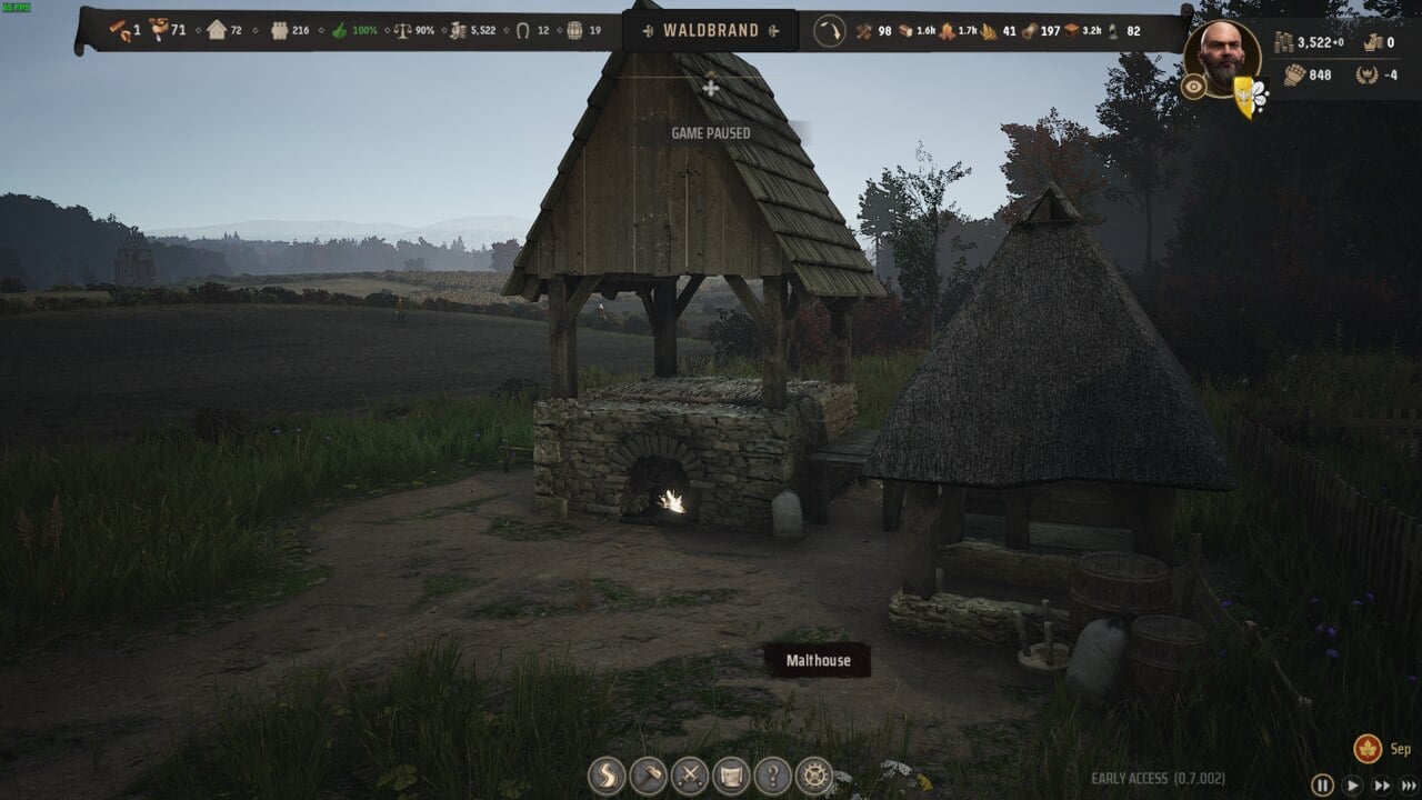 Manor Lords buildings: Screenshot from a video game featuring Manor Lords buildings, demonstrating a rustic medieval setting with a thatched-roof structure over a stone well and wooden shingle-roof house in a grassy field.