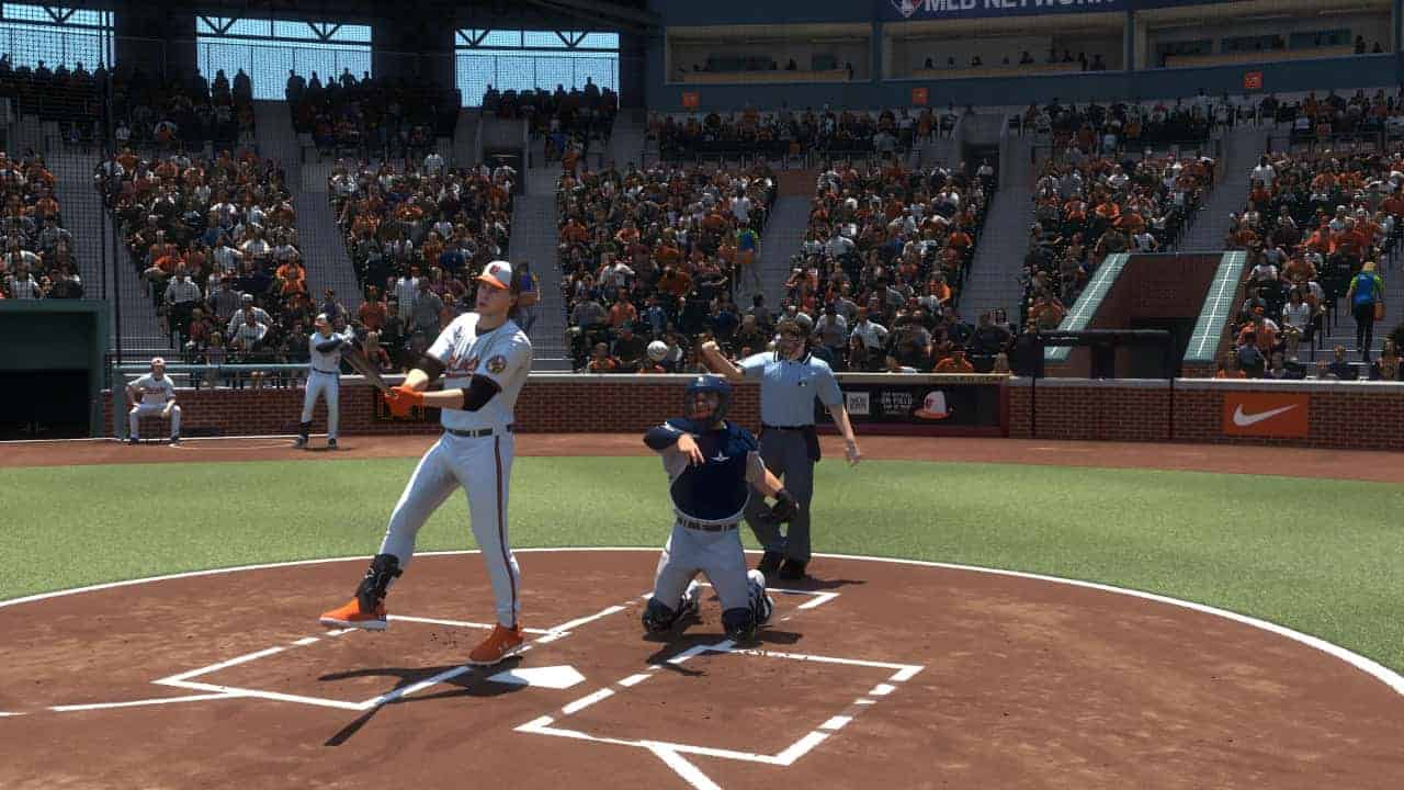 A baseball batter completing a swing at home plate with a catcher and umpire in the background within an MLB stadium.