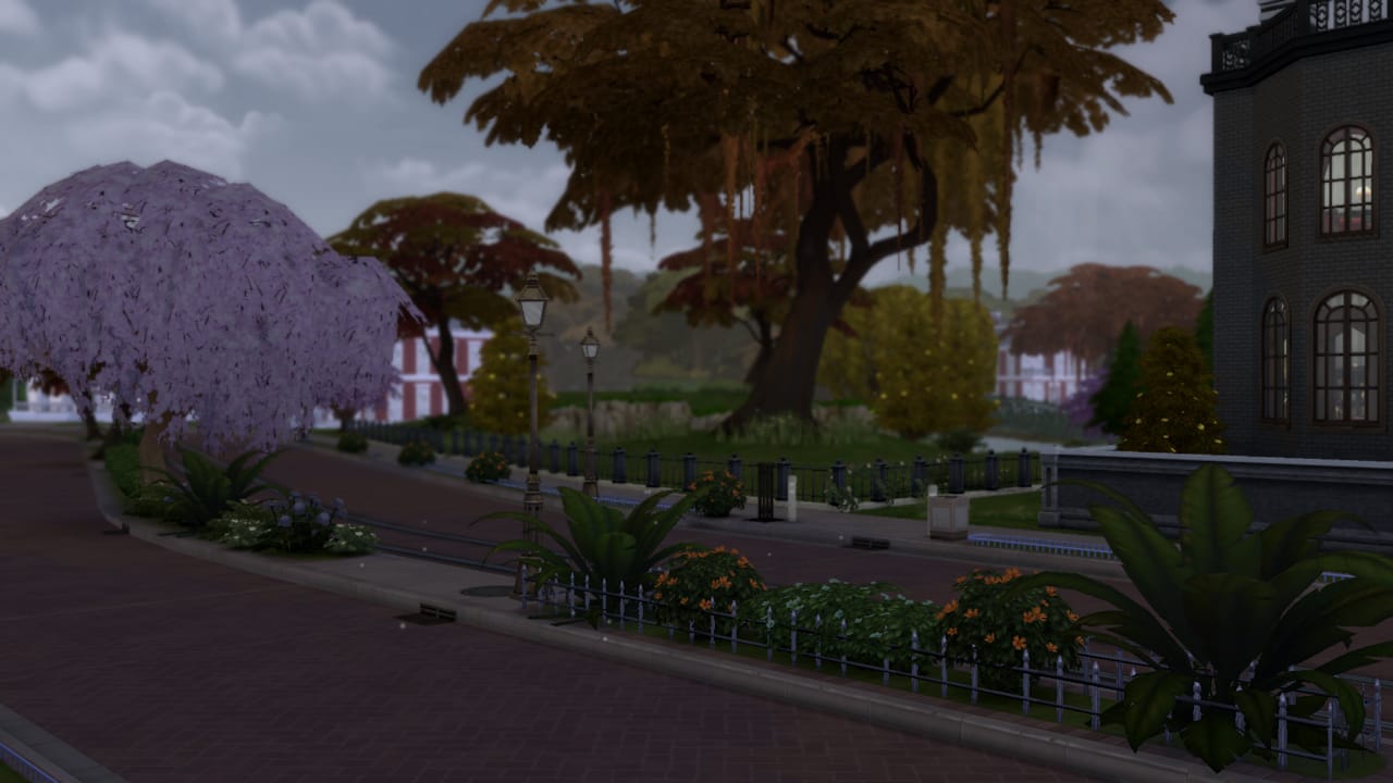 A *Sims 4* screenshot of a street with trees and buildings.