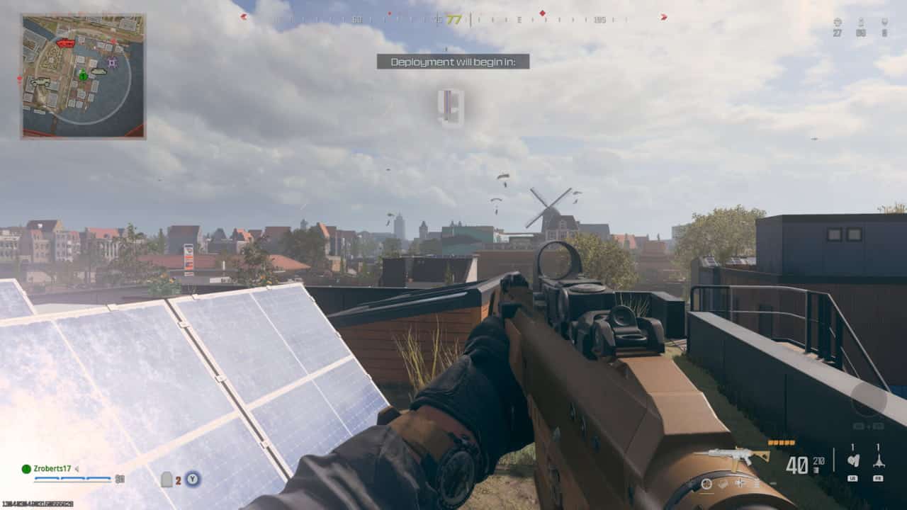 First-person perspective of a player holding a gun in a virtual battlefield environment with a countdown to deployment onscreen, exploring how to download Warzone mobile.
