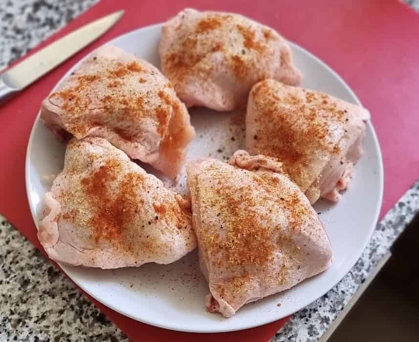 Raw chicken thighs on a plate with some paprika seasoning on.