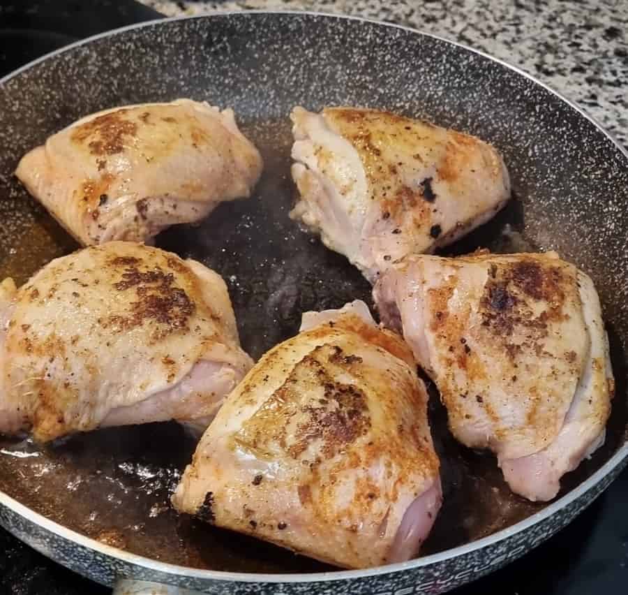 Five chicken thighs frying in a pan.
