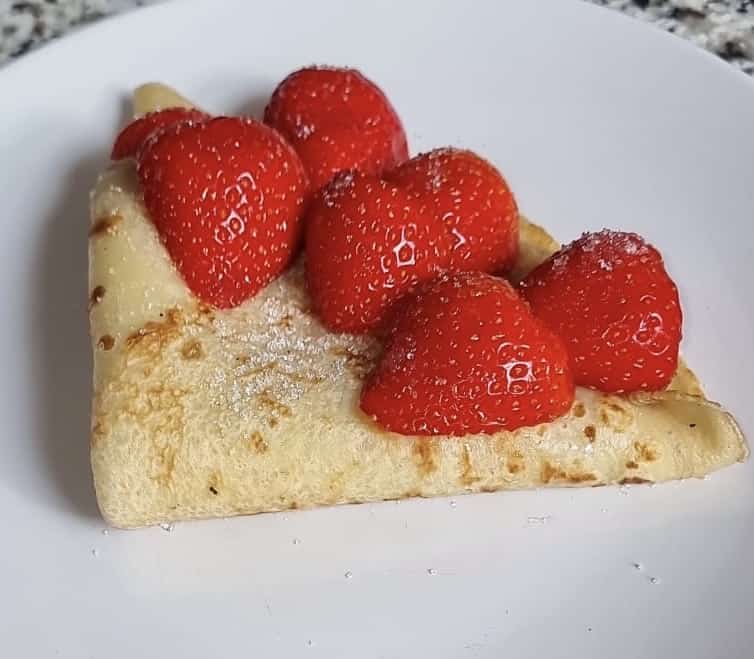 A crepe folded into a triangle with six strawberries on top.